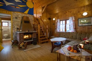 Interior acogedor de una cabaña con chimenea, paredes de madera, una escalera y un sofá.