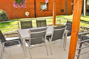 An outdoor seating area with a table and chairs, a wooden building in the background, and a hanging flower basket. - Four -anniversary Type B (Dzwirzyno)