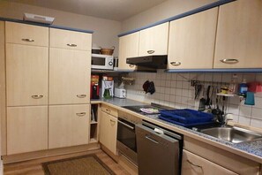 A compact kitchen with built-in appliances, wooden cabinets, and a stainless steel sink.