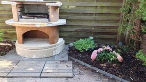An outdoor stone-built barbecue grill with a flat top, surrounded by a garden with hydrangeas and other greenery. - Holiday Home by the Baltic Sea with Terrace (Ostseebad Rerik)