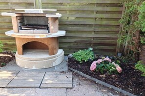 An outdoor stone-built barbecue grill with a flat top, surrounded by a garden with hydrangeas and other greenery. - Holiday Home by the Baltic Sea with Terrace (Ostseebad Rerik)