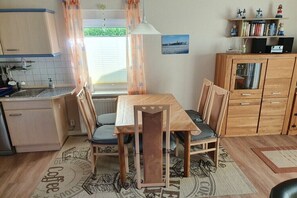 A compact kitchen with a dining table, chairs, a cabinet, and a window with curtains.