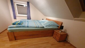 A single bed with a wooden frame, a bedside table with a lamp, and a window with curtains. - Holiday Home by the Baltic Sea with Terrace (Ostseebad Rerik)
