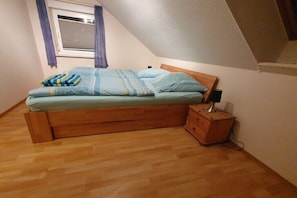 A single bed with a wooden frame, a bedside table with a lamp, and a window with curtains. - Holiday Home by the Baltic Sea with Terrace (Ostseebad Rerik)