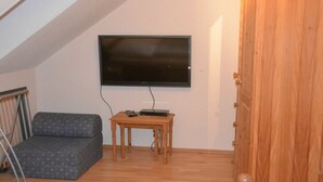 A room with a television mounted on the wall, a small wooden table, a grey patterned sofa, and a wooden door. - Holiday Home by the Baltic Sea with Terrace (Ostseebad Rerik)
