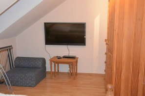 A room with a television mounted on the wall, a small wooden table, a grey patterned sofa, and a wooden door. - Holiday Home by the Baltic Sea with Terrace (Ostseebad Rerik)