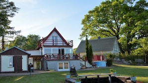 Ein zweistöckiges Haus mit Balkon, einer kleinen Werkstatt und einem gepflegten Rasen mit Gartenmöbeln.