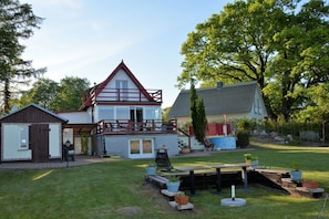A two-story house with a balcony, a small shed, and a well-maintained lawn with outdoor furniture. - Chalet by Lake with Sauna and Hot Tub (Krakow am See)