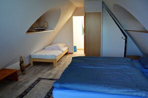 A bedroom with a sloped ceiling, a bed with striped bedding, a small wooden bench, and a ship model on the wall.
