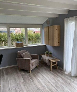 Relax in a cozy seating area with a striped armchair and small table, overlooking lush greenery through a large window.