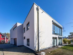Une maison moderne à deux étages, avec une façade blanche, de grandes fenêtres et un toit en pente.