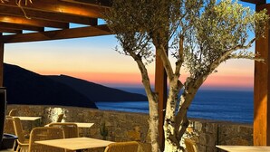An outdoor seating area with tables and chairs, overlooking a scenic view of the sea and hills during sunset. - Maison Meltem (Malevizi)