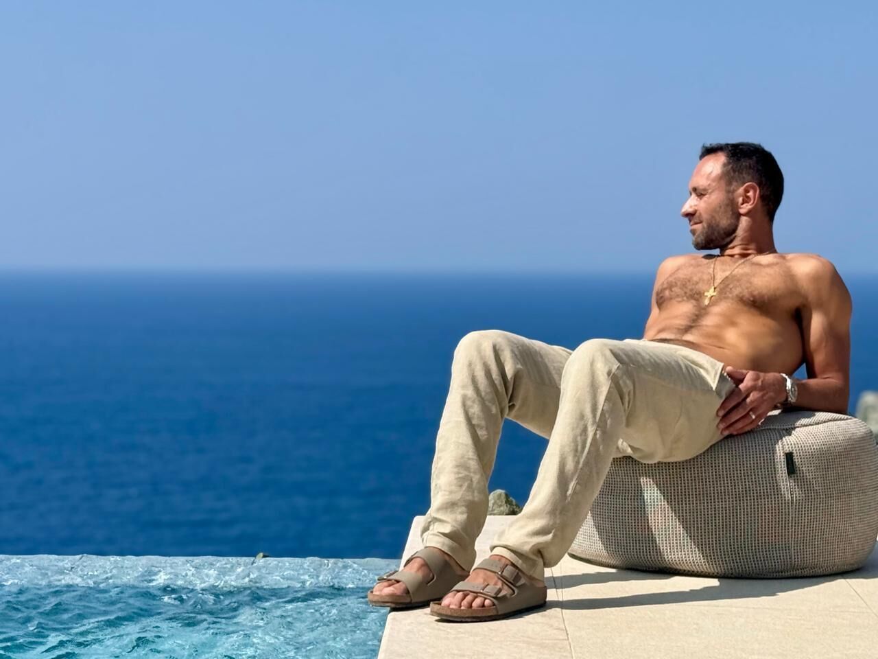 A man sitting on a bean bag chair by a pool with a view of the ocean.