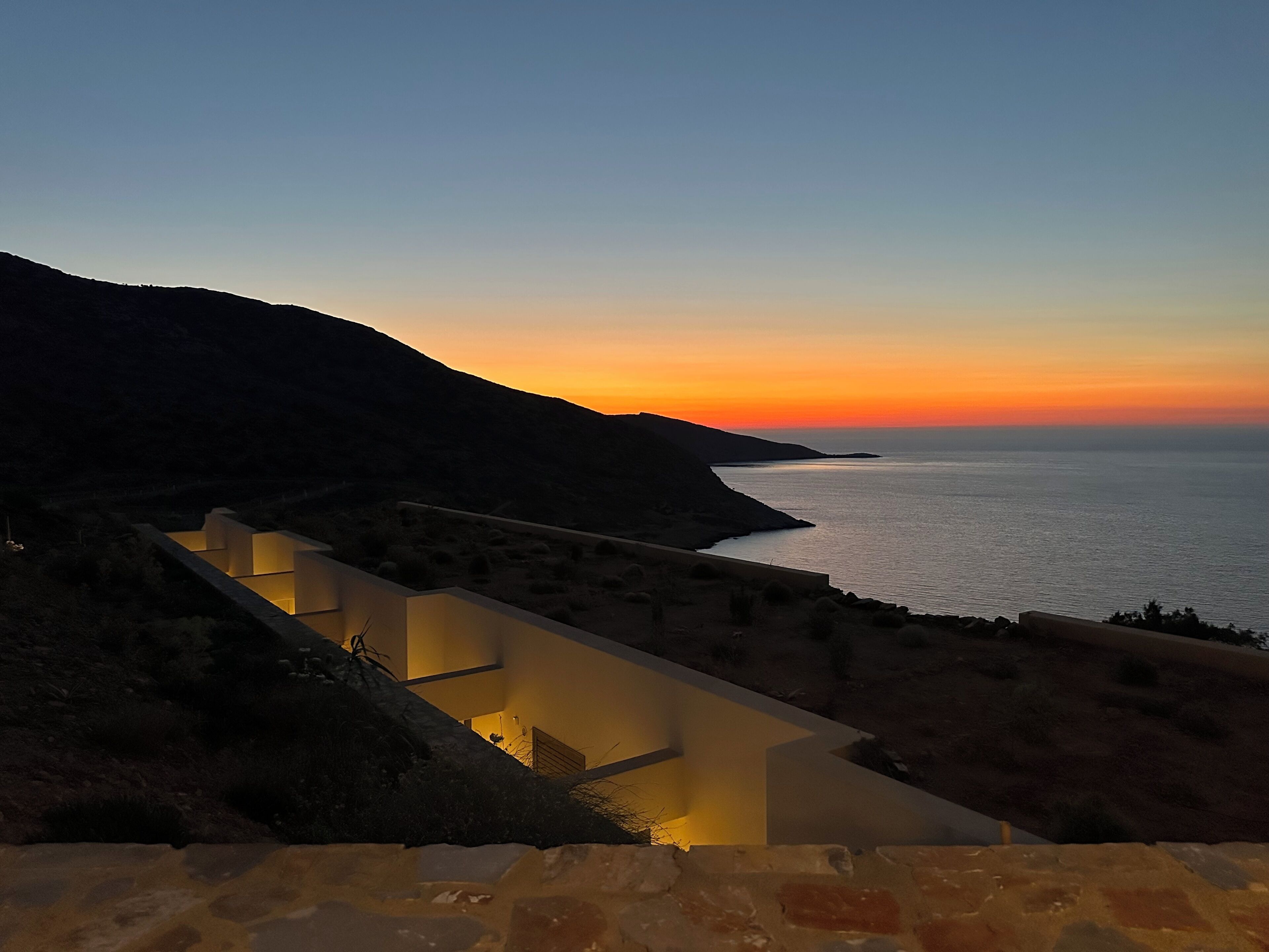 A coastal landscape with a modern building featuring a zigzag design, overlooking the sea during sunset.