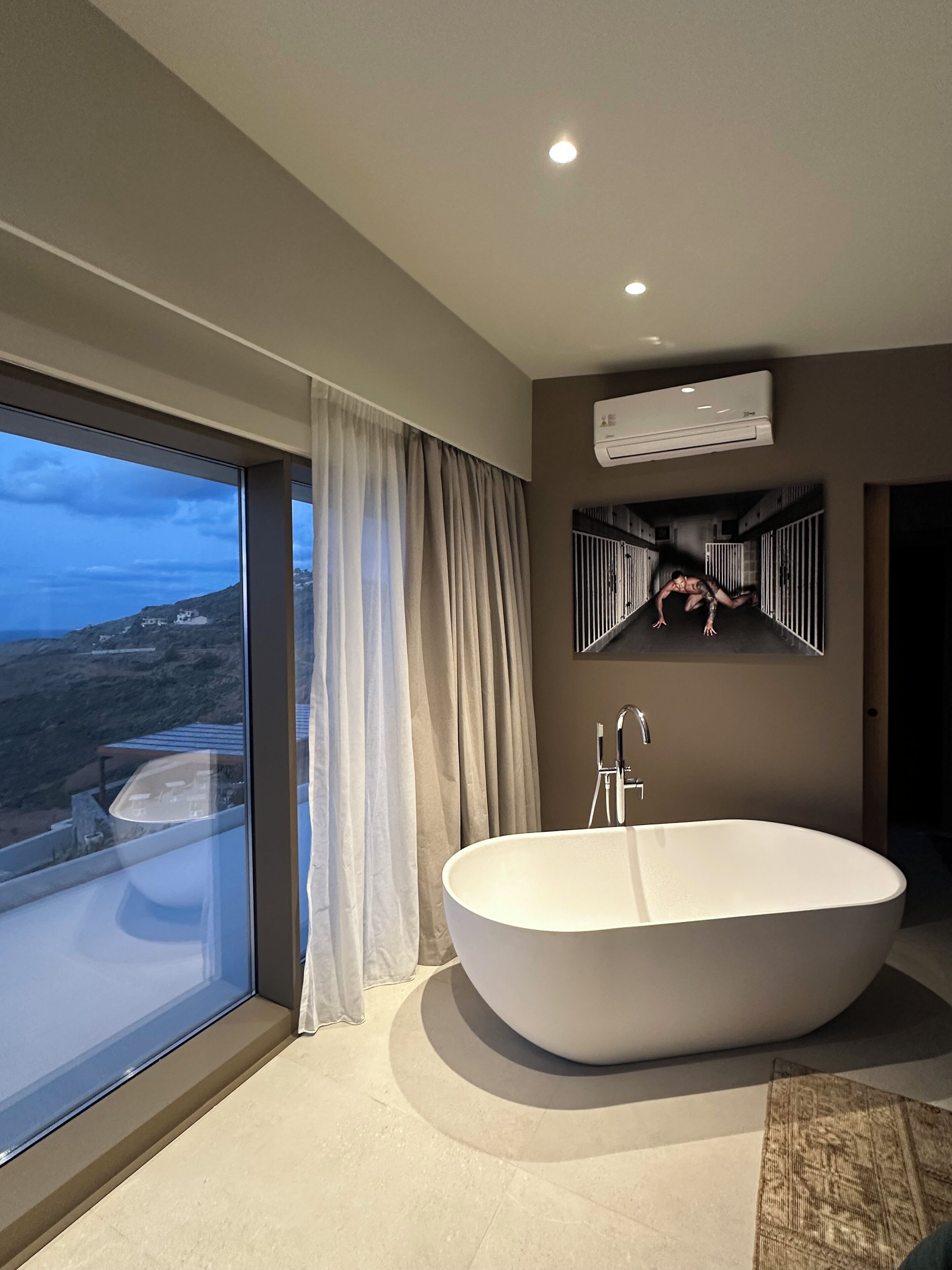 Une salle de bain moderne avec une baignoire sur pieds, une grande fenêtre avec des rideaux et un climatiseur fixé au mur.