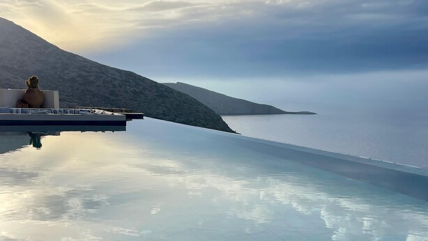 A clear blue infinity pool with a view of the sea and a mountain in the background. - Maison Meltem (Malevizi)