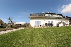 Ein zweistöckiges Haus mit großem Vorgarten, einem Weg zum Eingang und blauem Himmel.