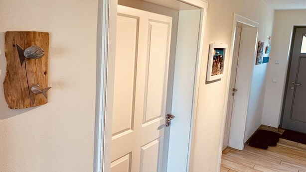 A hallway with a wooden wall decoration, a white door, and a framed picture on the wall.