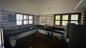 A kitchen with a gas stove, microwave, and refrigerator. There are windows with bars, a sink, and a trash bin.