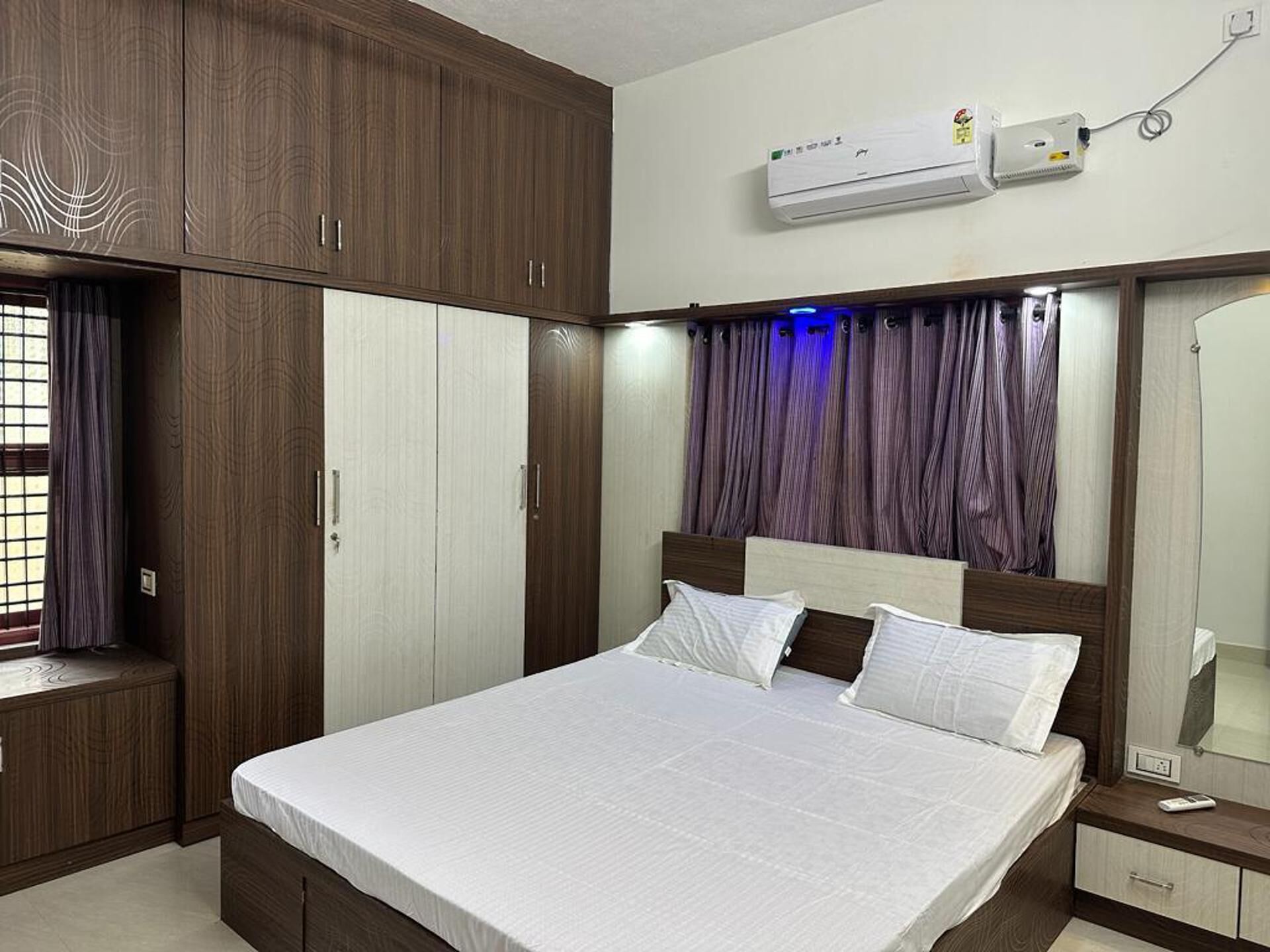 A hotel room with a large bed, wooden wardrobe, and an air conditioning unit.