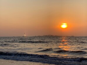 A sunset over the ocean with waves and a distant landmass.
