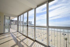 Un balcon spacieux avec de grandes fenêtres donnant sur une plage et sur le paysage urbain.