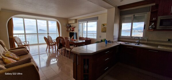 Un vaste espace de vie doté d’une grande fenêtre offrant une vue sur la mer, une table à manger avec des chaises et un canapé de la marque Galaxy S22 Ultra.