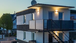 Een modern meerlaags gebouw met een plat dak, een balkon op de bovenste verdieping en een trap naar het hogere niveau.