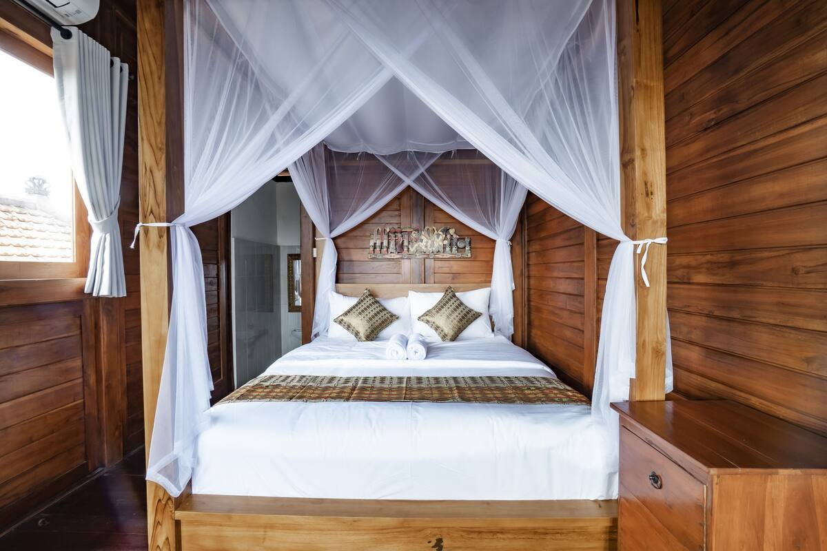 A wooden four-poster bed with a canopy, white bedding, and decorative pillows.