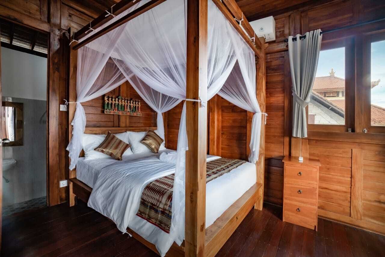 A four-poster bed with white linens, a wooden headboard, and a mosquito net.