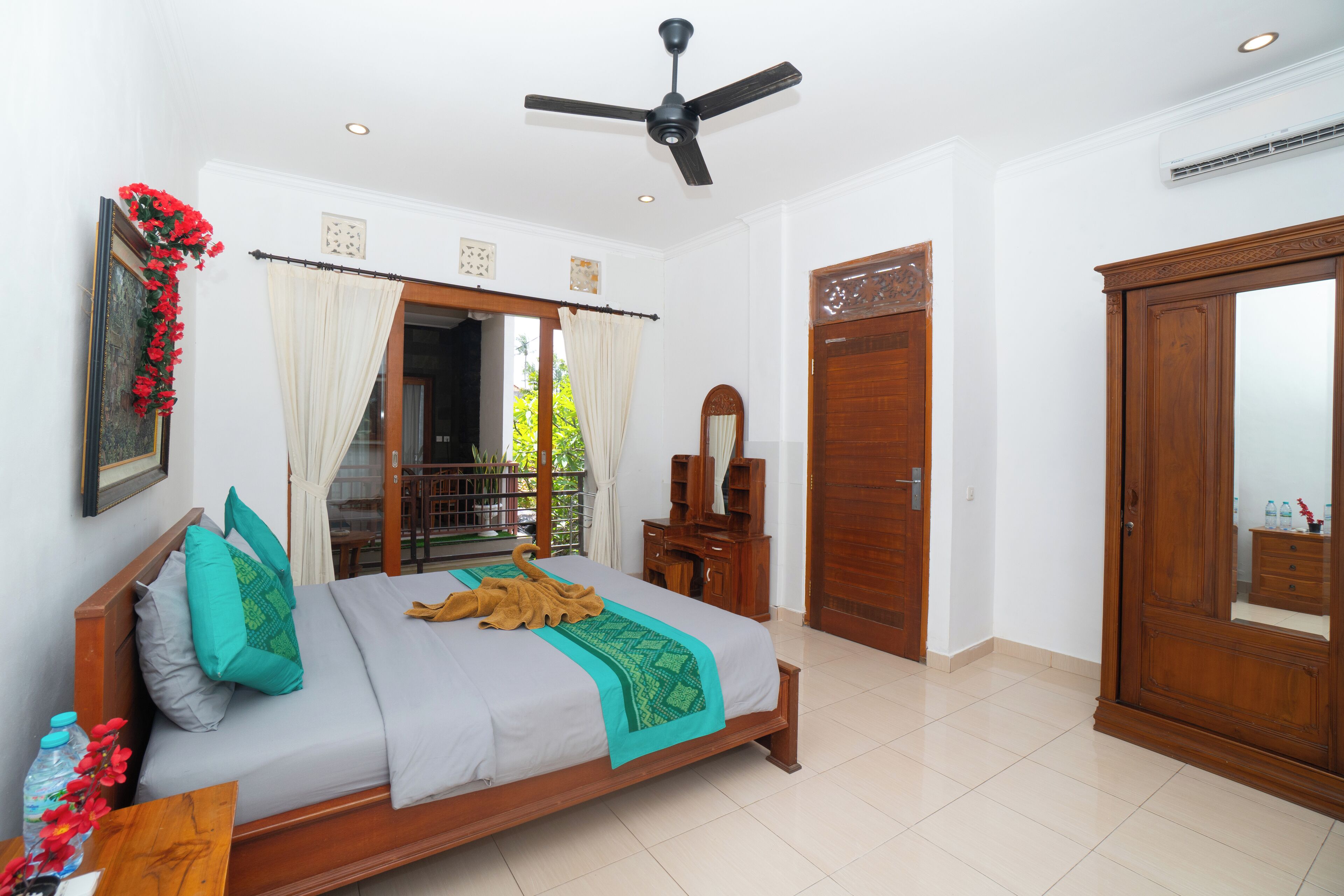 A bedroom with a bed, wooden wardrobe, ceiling fan, and a view of the outdoors.