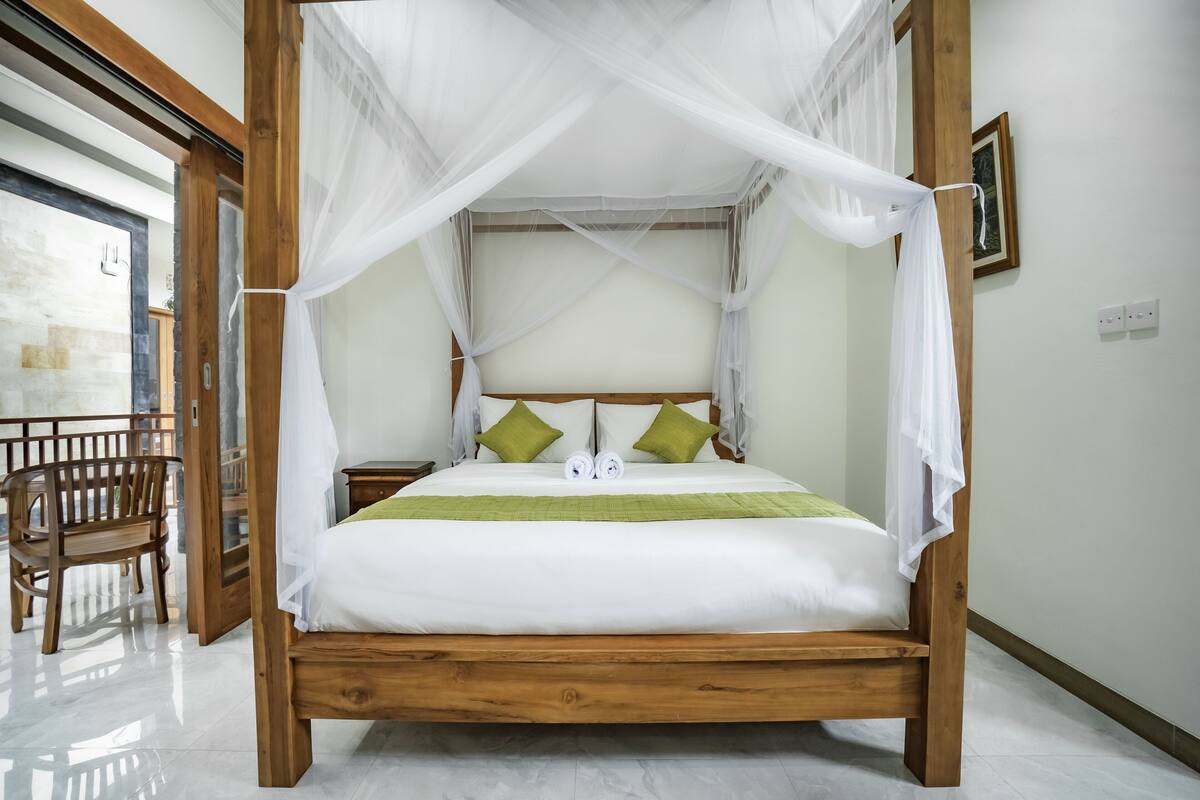 A four-poster bed with white bedding and green pillows, a wooden headboard, and a canopy.