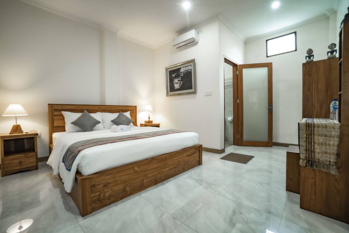 A bedroom with a wooden bed, two bedside tables with lamps, a large mirror, a wardrobe, and a framed picture on the wall.