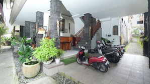 Un espacio al aire libre techado con pilares de piedra, una moto roja y plantas en macetas.