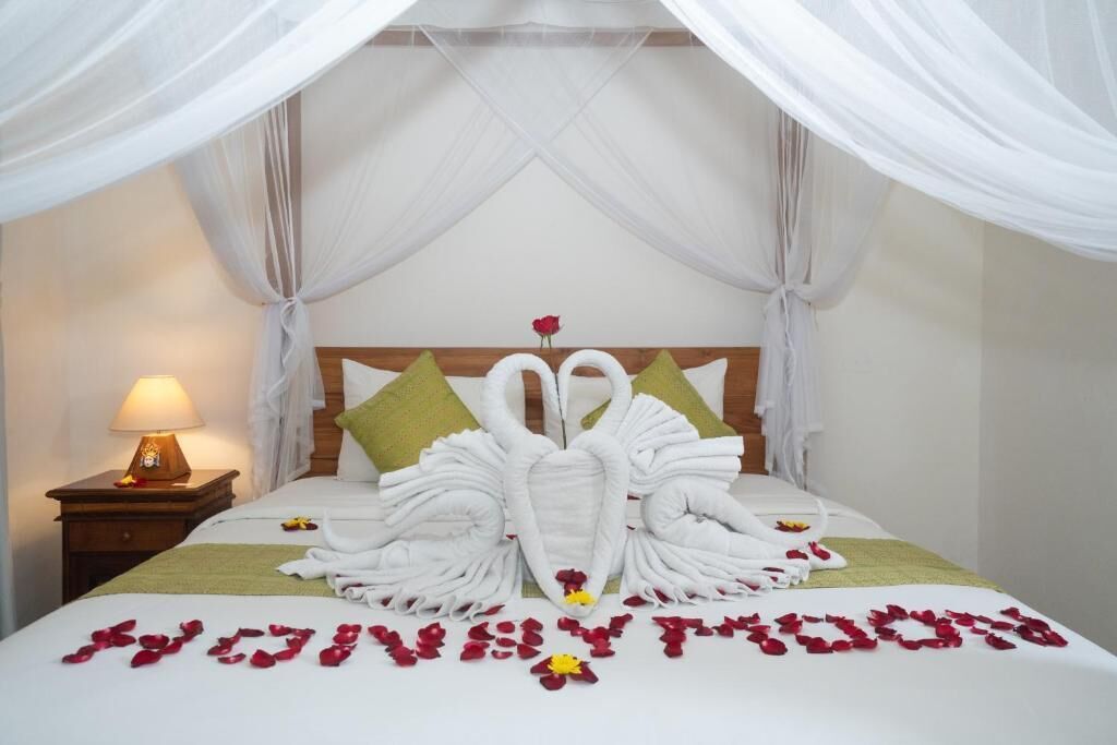 A hotel room with a bed adorned with swan-shaped towels and rose petals spelling 'LOVE YOU' on the bedspread.
