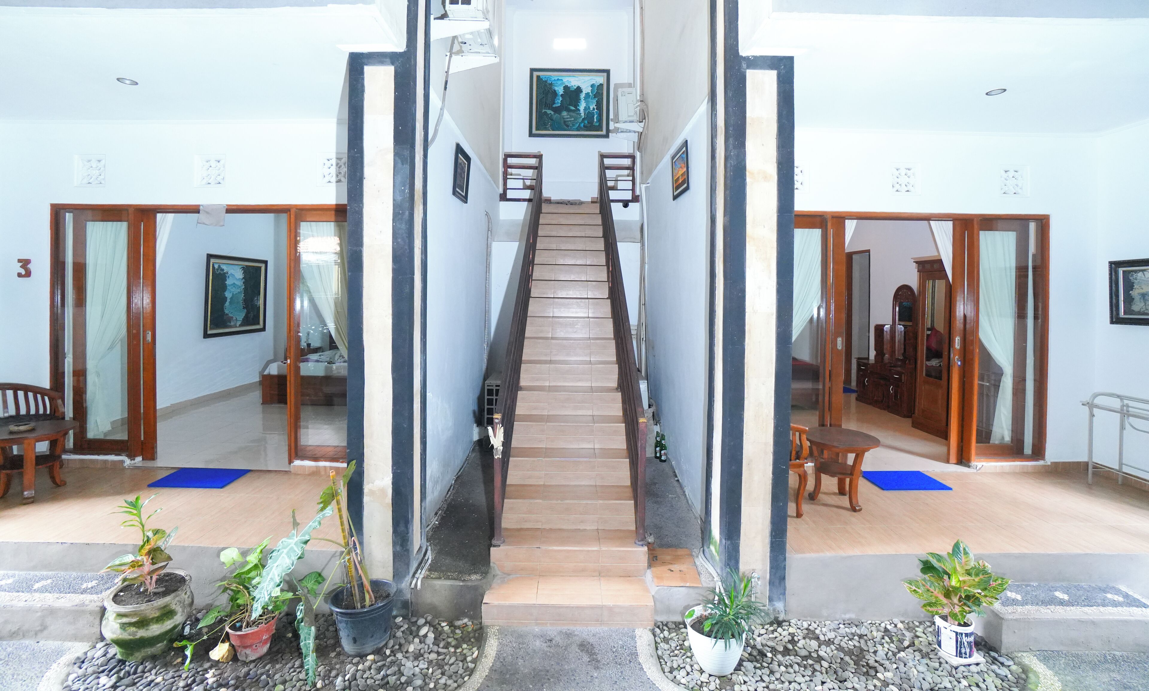 Vestíbulo de hotel con una escalera central, plantas en macetas y un felpudo azul en el suelo.