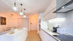 A modern kitchen with white cabinetry, a central island, pendant lighting, and a view into the dining area.