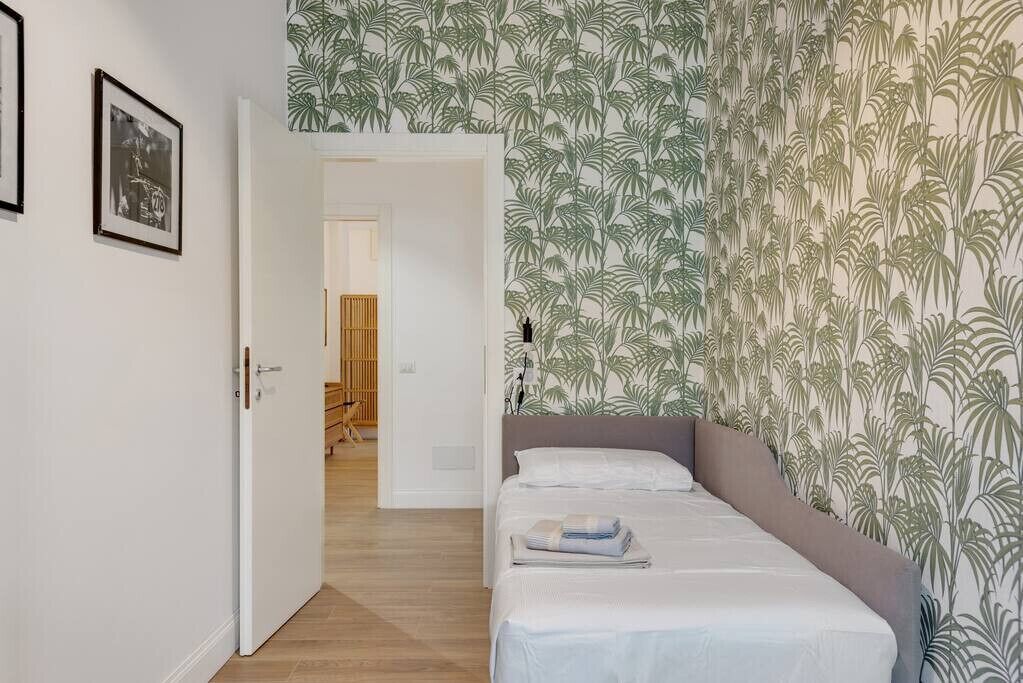 Une chambre à coucher avec un lit, une porte et un mur orné d’un motif de feuilles tropicales.