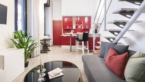 A modern living room with a sofa, a coffee table, and a dining area with red cabinets and a kitchen in the background. - Easylife - Cozy studio in Via Torino, perfect location to visit the city (Milano)