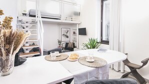 A modern, well-lit room with a bunk bed, a dining table with placemats, a plant, and a window with curtains. - Easylife - Cozy studio in Via Torino, perfect location to visit the city (Milano)