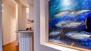 Un pasillo con un radiador blanco, un lavamanos y un cuadro enmarcado con peces en la pared.