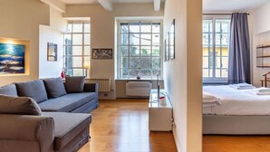 Una habitación de hotel moderna con sofá, cama, radiador y ventana con cortinas.