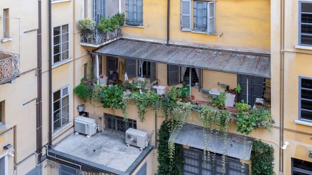 Un edificio de varios pisos con balcones, mobiliario exterior y vegetación.