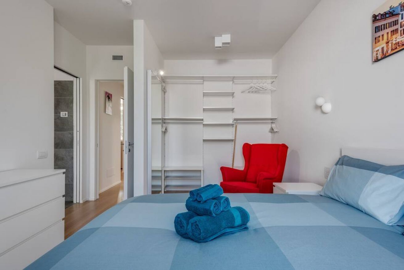 A bedroom with a bed, a red chair, and a wardrobe.