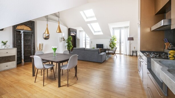 Een moderne keuken met een ingebouwde kookplaat, houten vloer en een eethoek met een tafel en stoelen.