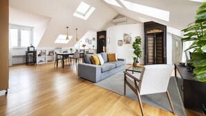 Een ruime loftappartement met een hoge plafon, dakramen, een eetgedeelte en een woonkamer met een grijze bank en een salontafel.