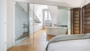 Een moderne slaapkamer met een glazen deur naar een balkon, een groot bed en een marmeren badkuip.
