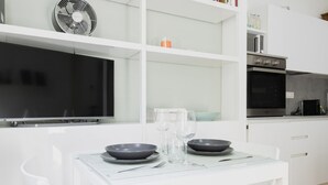 A modern kitchen with white cabinetry, a built-in oven, and a microwave. There is a dining table with two bowls and wine glasses. - Easylife - Elegance and Comfort in the Isola area (Milano)
