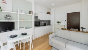 A modern living room with a grey sofa, a dining table with chairs, and a kitchen area with white cabinets and appliances. - Easylife - Elegance and Comfort in the Isola area (Milano)