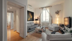 Una sala moderna con un sofá gris, un sillón blanco, una mesita de centro y un televisor.